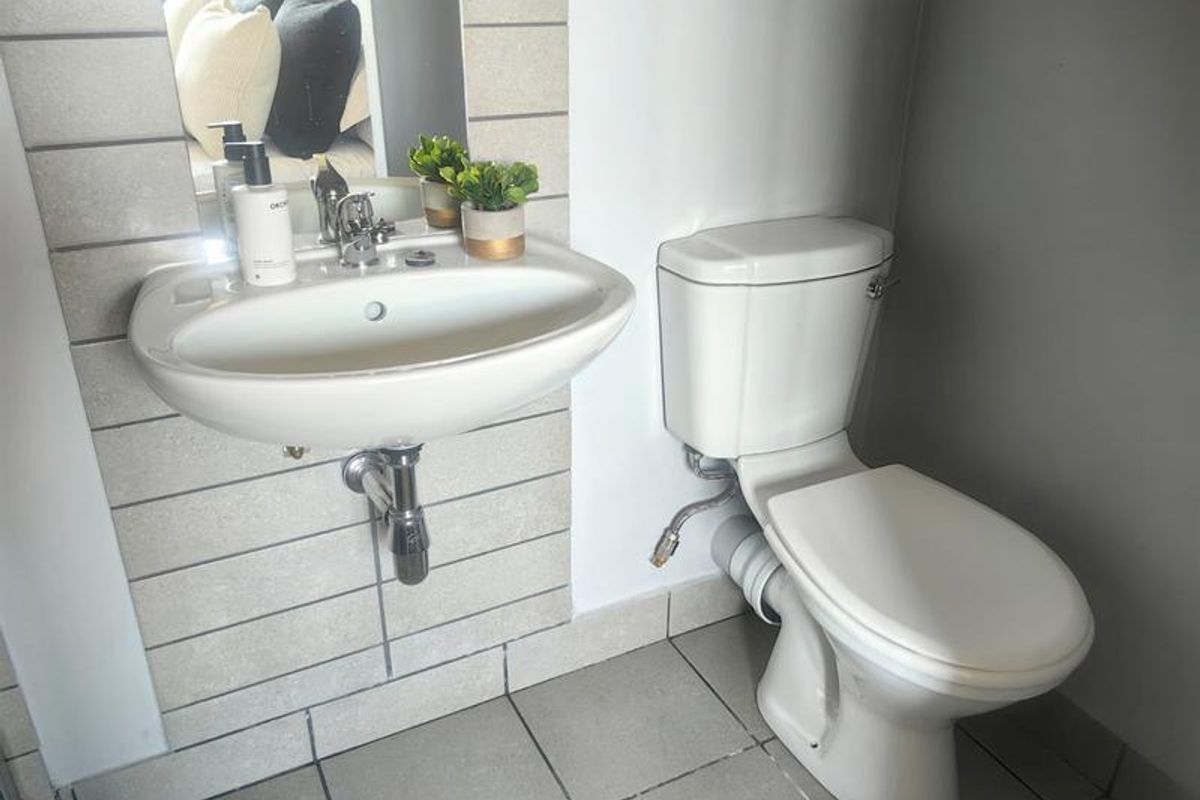 A compact bathroom featuring a wall-mounted basin with chrome fixtures and a standard toilet, finished with tiled splashbacks and flooring.