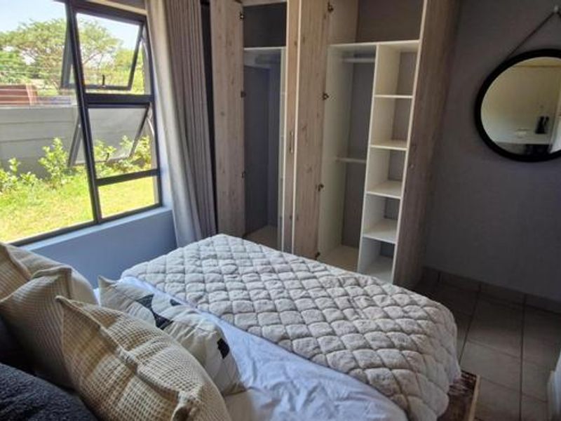 A well-lit bedroom featuring modern built-in cupboards, tiled flooring, and large aluminium-framed windows overlooking the garden area.