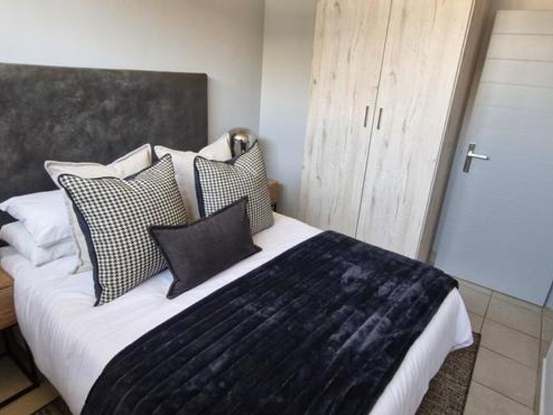 A well-maintained bedroom featuring neutral tiled flooring, a built-in wardrobe with wood-grain finish, and a modern internal door.