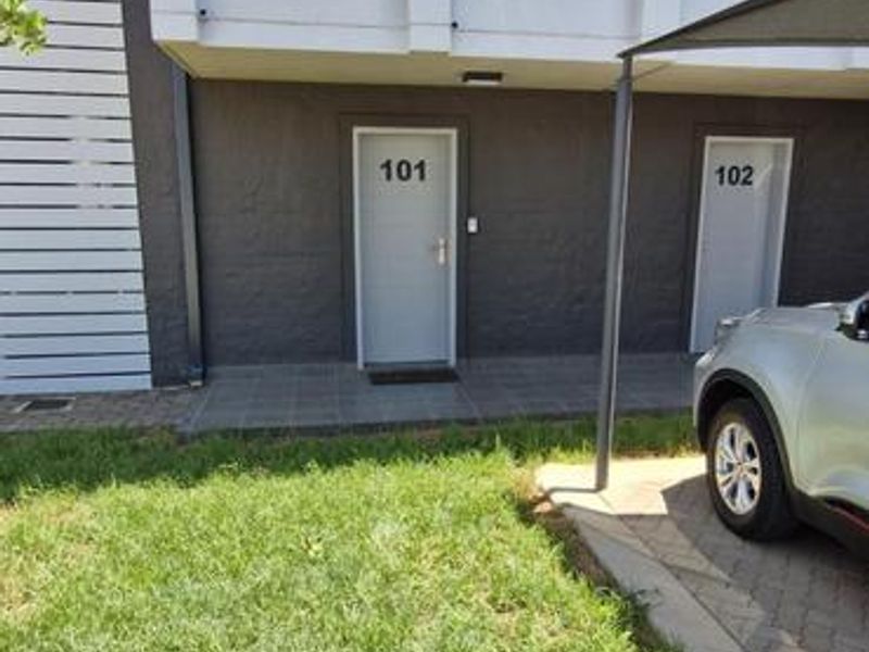 Exterior view of apartment unit 101, featuring a paved entrance area, modern dark facade, and well-maintained lawn.