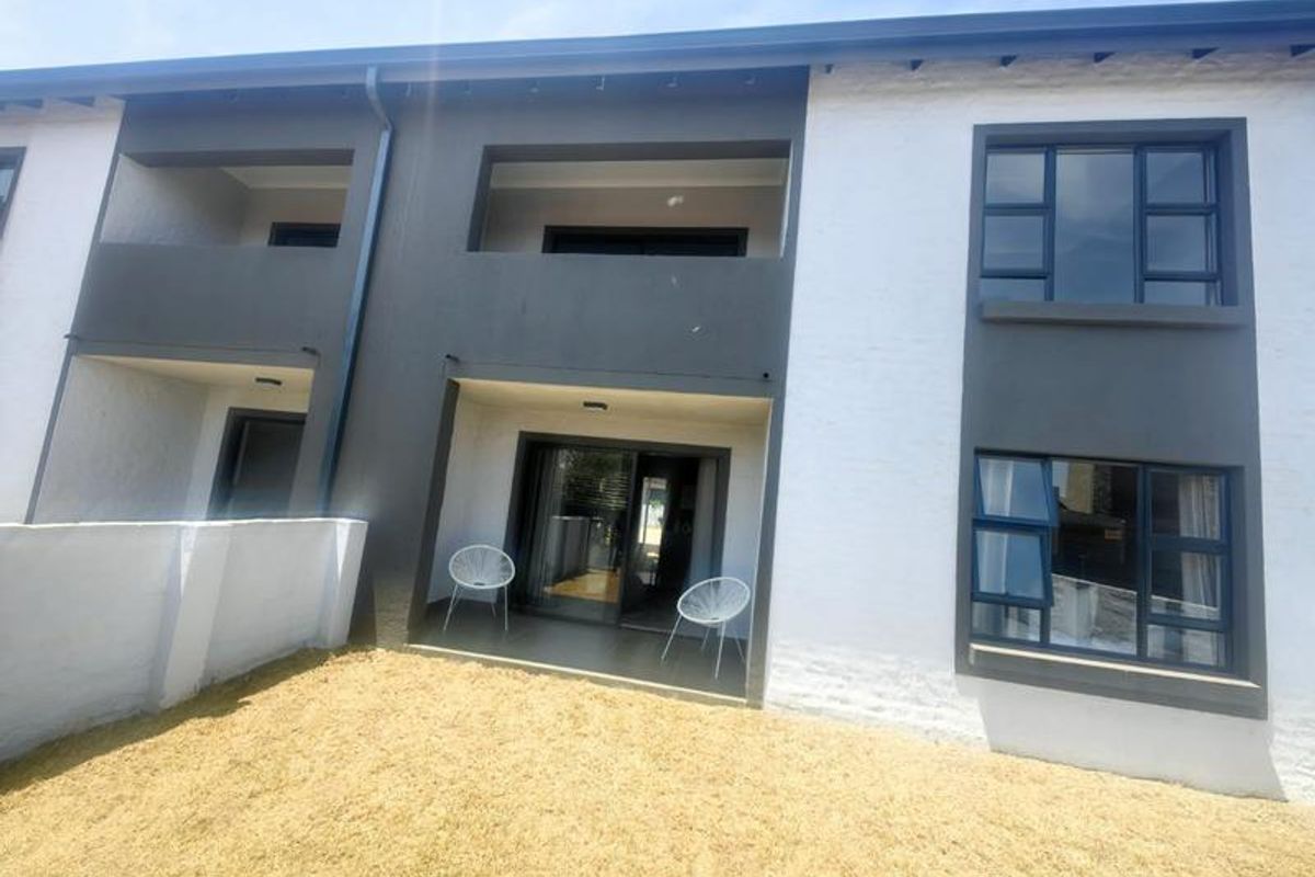Rear view of a modern apartment building featuring a covered patio, sliding glass doors, and a small private garden area.