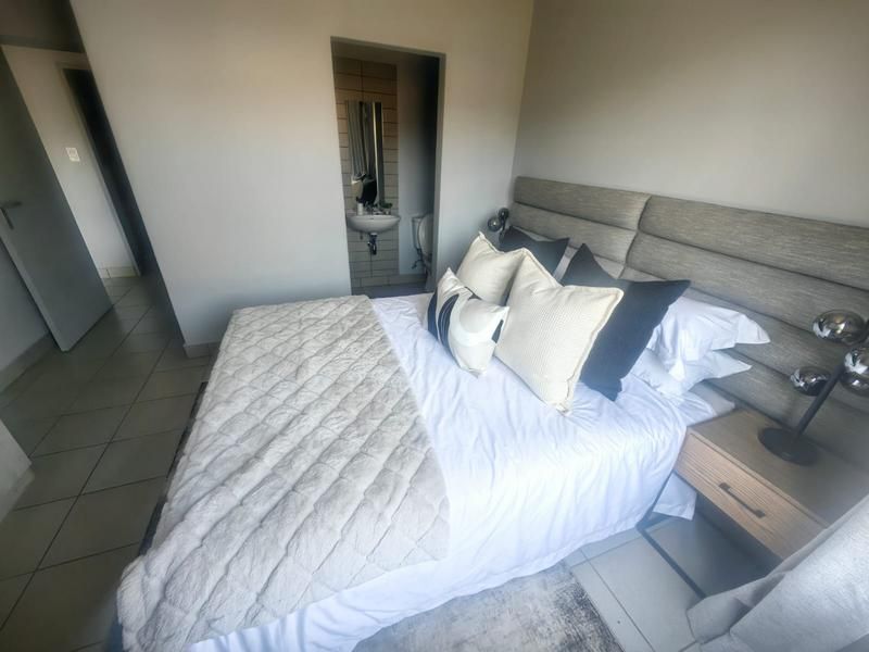 A well-maintained bedroom featuring tiled flooring, a modern wall-mounted headboard, and an integrated en-suite bathroom.