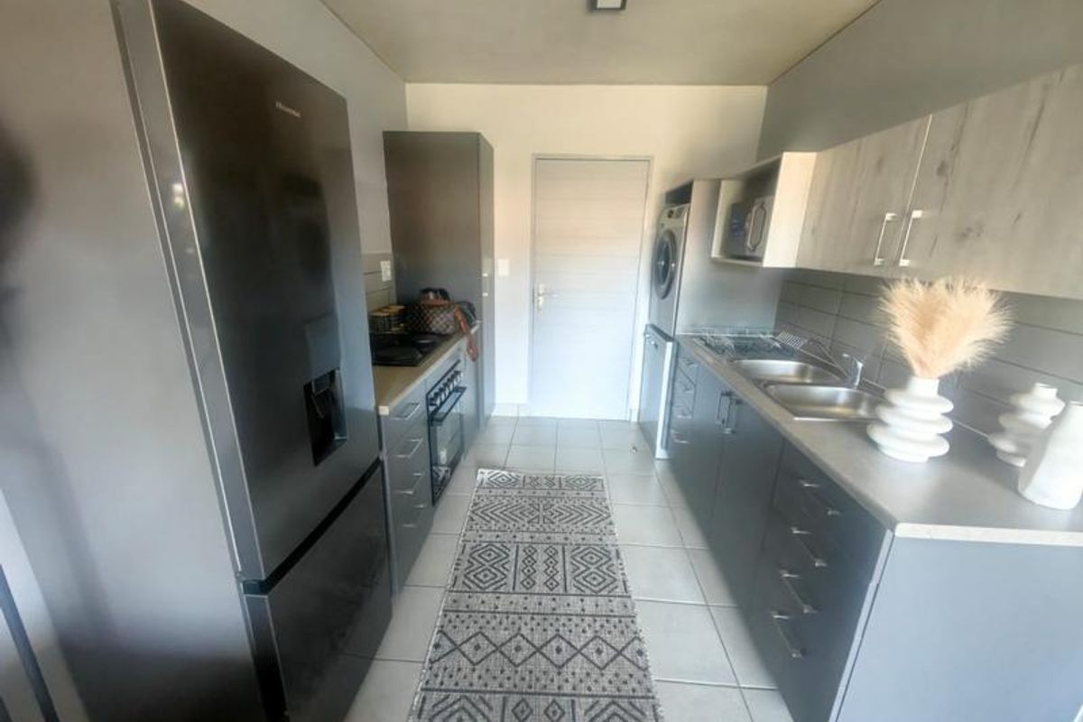 Modern kitchen featuring sleek grey cabinetry, double sink, built-in oven, hob, and dedicated space for laundry appliances with neutral tiled flooring.