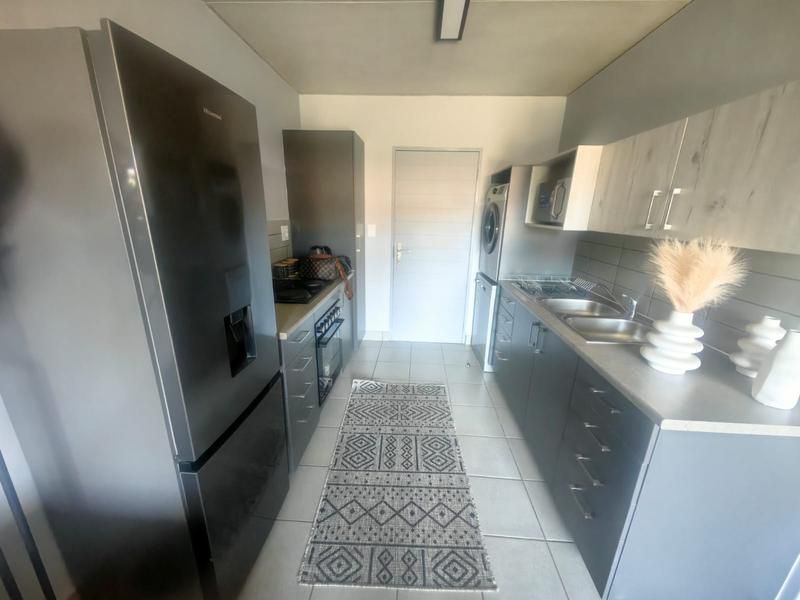 Modern kitchen featuring sleek grey cabinetry, double sink, built-in oven, hob, and dedicated space for laundry appliances with neutral tiled flooring.