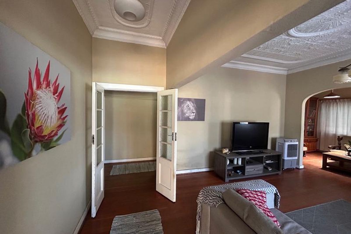 Spacious living area featuring classic ornate plaster ceilings, hardwood flooring, and an elegant archway leading to an adjacent room.