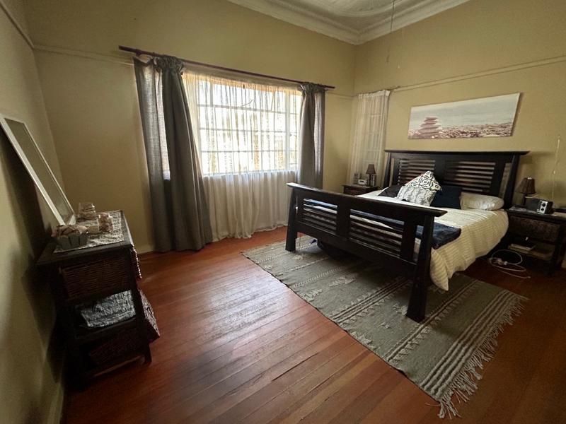 A spacious bedroom featuring original hardwood flooring, ornate ceiling cornicing, and large windows allowing for natural light.