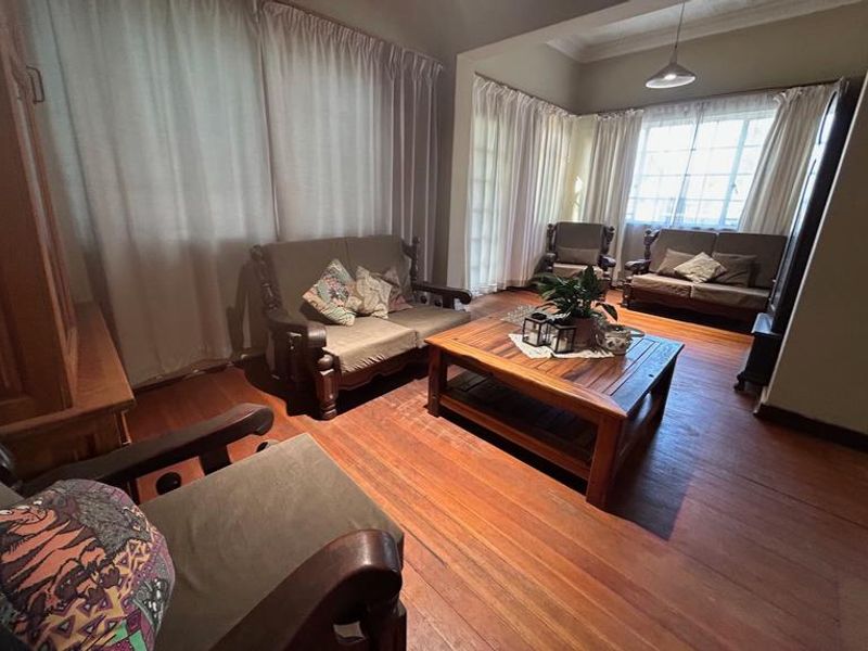 A cozy living room featuring warm hardwood flooring, coved ceilings, and large windows that allow for natural light.