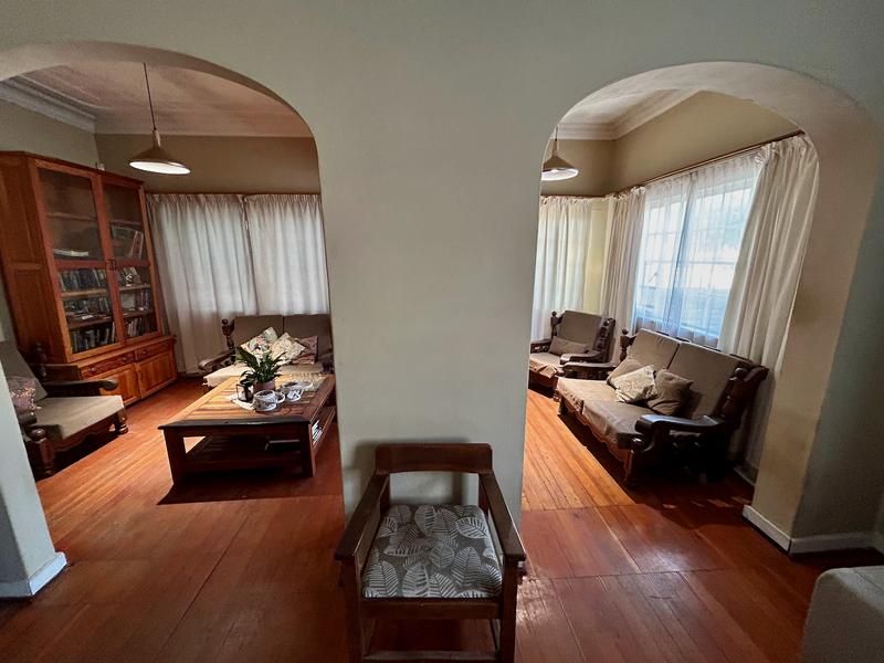 Spacious living area featuring original hardwood flooring, distinctive arched doorways, and coved ceilings, offering a classic architectural layout.