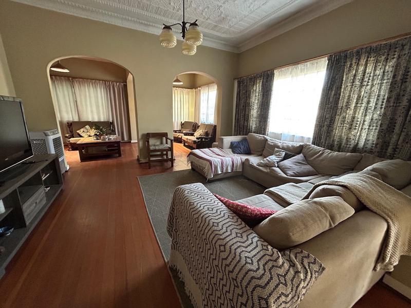 Spacious living room featuring original hardwood flooring, decorative ceiling details, and classic archways connecting to adjacent living areas.
