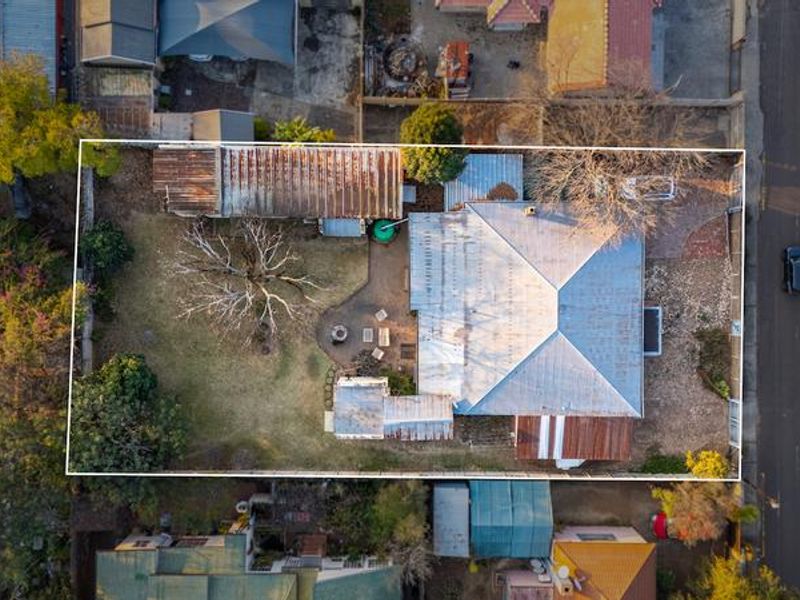 Aerial view of the property showing the main house with a corrugated metal roof, surrounding garden, and rear outbuildings on the plot.