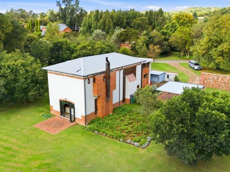 Aerial view of a well-maintained small holding property featuring a brick and white-walled dwelling with a metal roof, set within a lush garden.