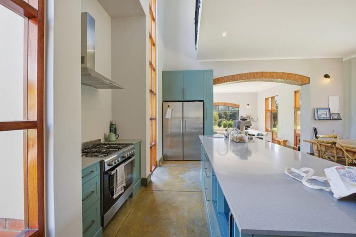 Modern kitchen featuring a large stone-topped island, gas stove with extractor, custom cabinetry, and polished concrete floors, opening into a spacious living area.
