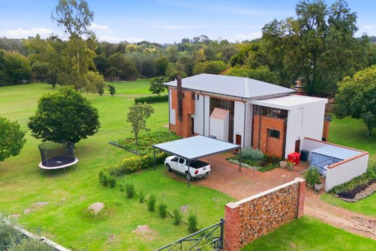 Aerial view of a multi-story small holding property featuring a metal roof, brick exterior, carport, and expansive landscaped grounds.