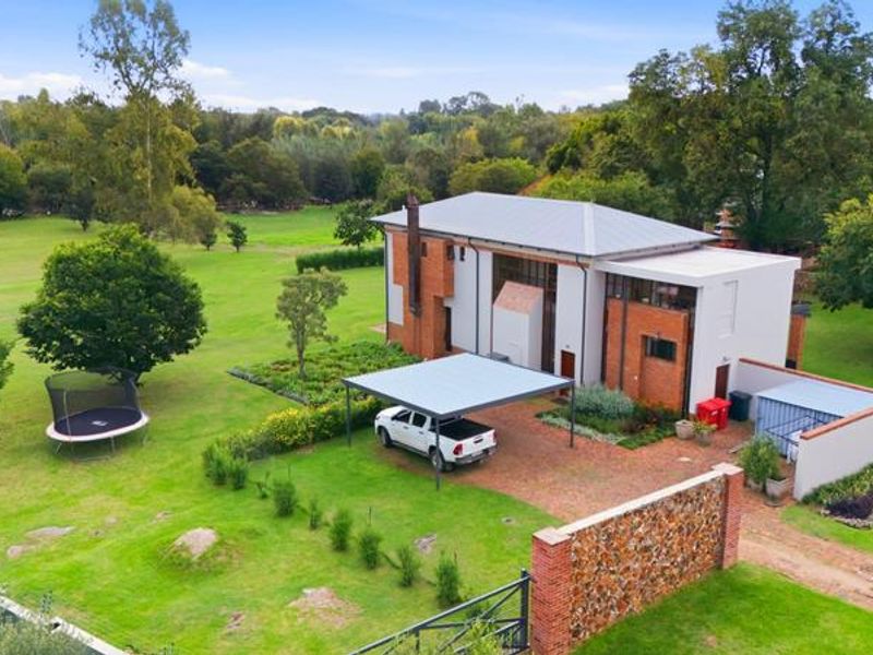 Aerial view of a multi-story small holding property featuring a metal roof, brick exterior, carport, and expansive landscaped grounds.