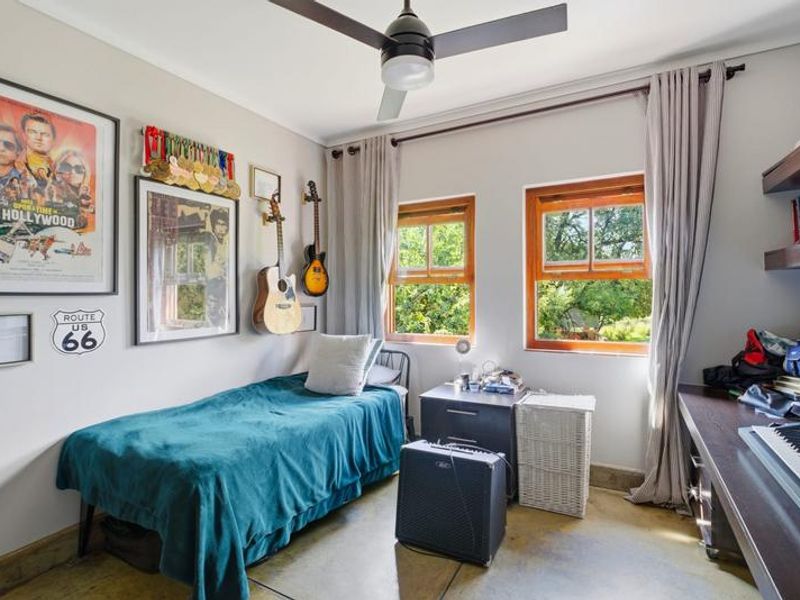 A well-lit bedroom featuring polished concrete flooring, wooden window frames, a ceiling fan, and built-in shelving units.