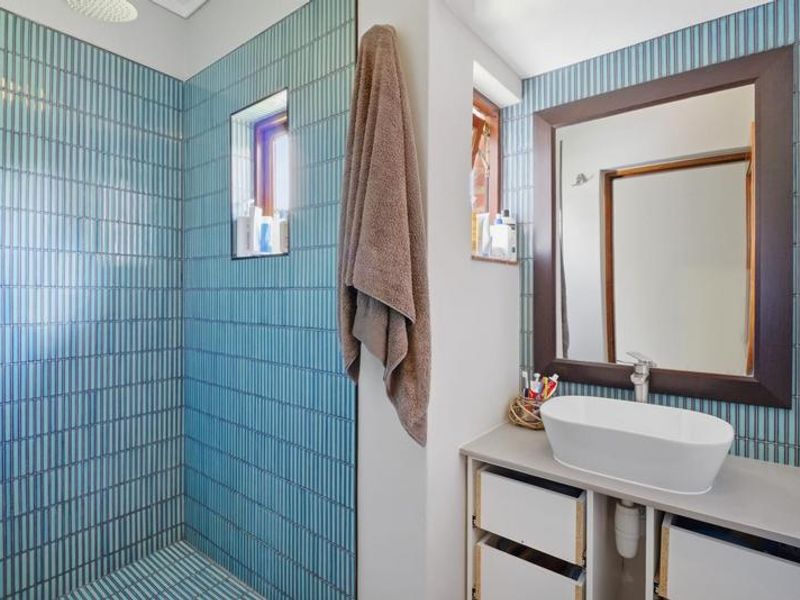 Modern bathroom featuring a walk-in shower with blue vertical tiling, a rain shower head, and a contemporary vanity with a vessel sink.