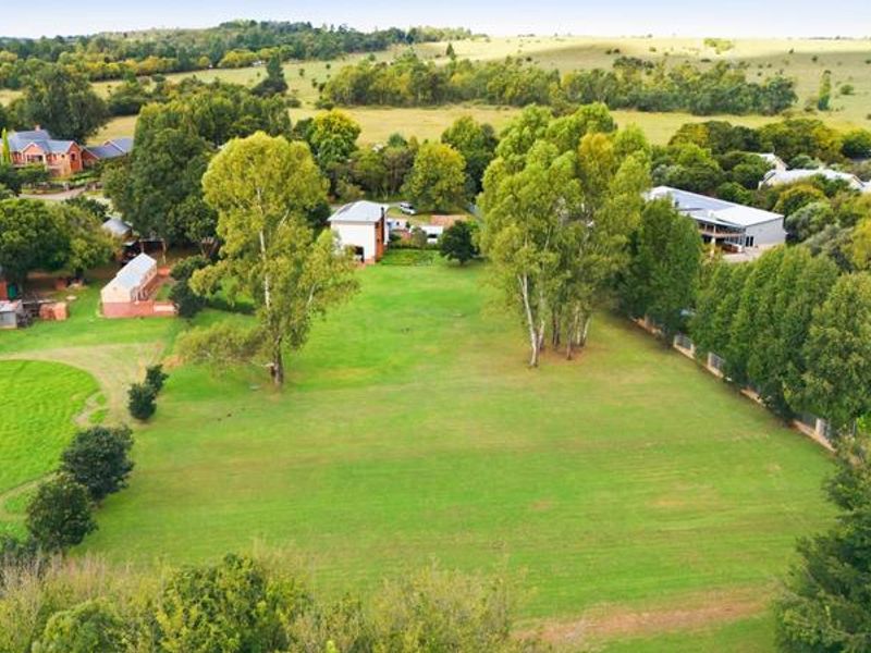 An aerial view of a spacious small holding property featuring expansive green lawns, mature trees, and surrounding rural landscape.