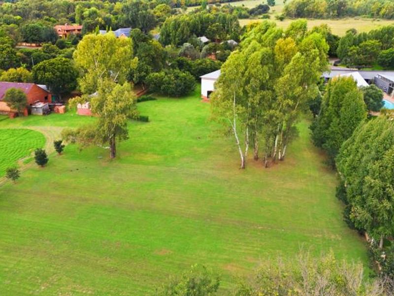 Aerial view of a spacious small holding property featuring expansive green lawns, mature trees, outbuildings, and a swimming pool area.