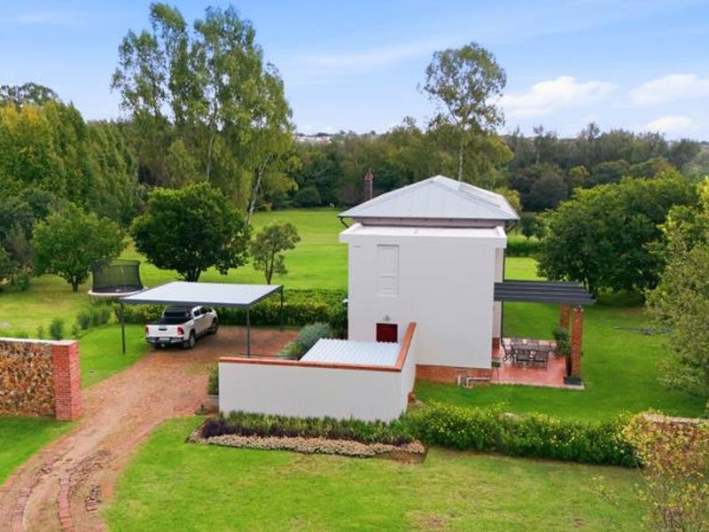 Aerial view of a small holding property featuring a modern dwelling, a carport, a covered patio, and expansive green garden spaces.