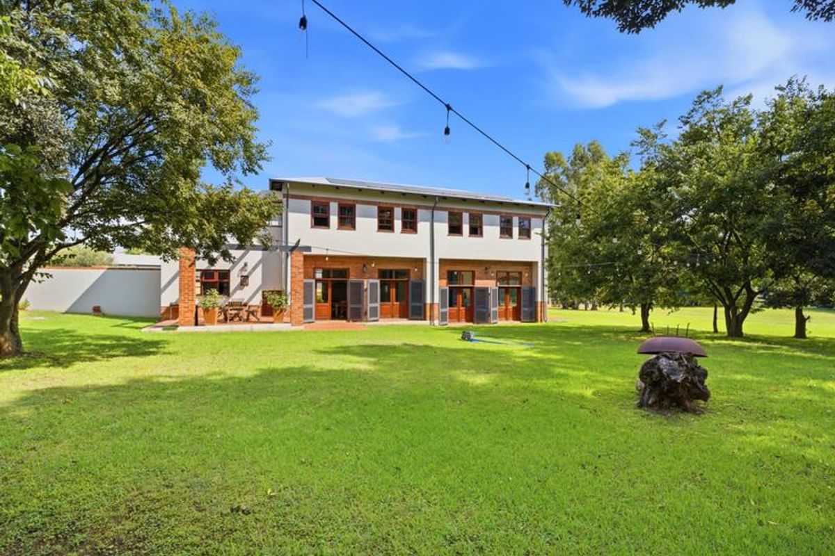 Rear view of a two-story brick and plaster residence featuring a paved patio, large lawn, and mature trees.