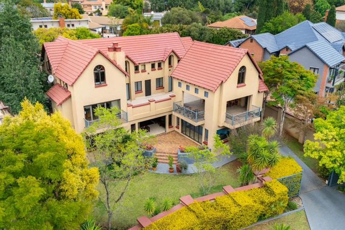 Aerial view of a multi-story residential property featuring a tiled roof, multiple balconies, and a paved patio area set within a landscaped garden.