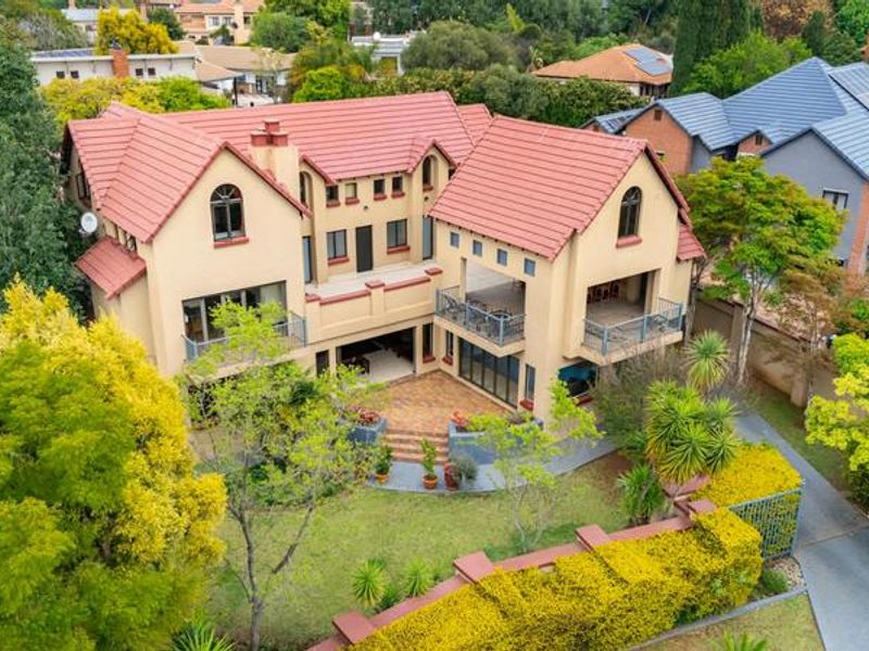 Aerial view of a multi-story residential property featuring a tiled roof, multiple balconies, and a paved patio area set within a landscaped garden.