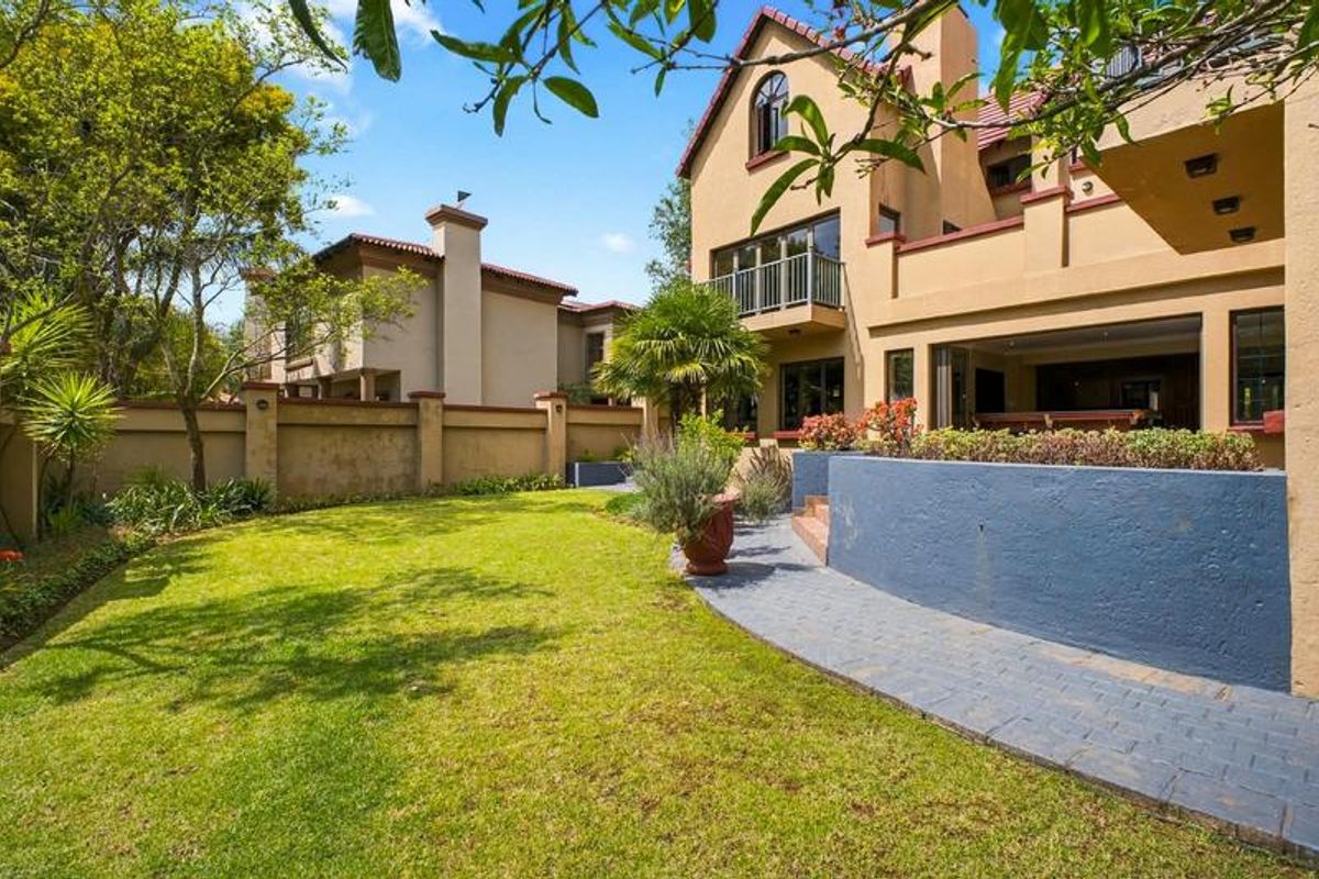 Rear view of the property featuring a landscaped garden, paved walkway, and a multi-story building with a balcony and tiled roof.