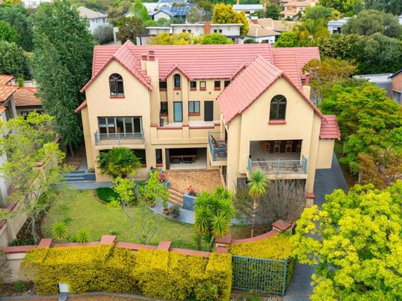 Aerial view of a multi-story residential property featuring a tiled roof, multiple balconies, a paved patio area, and a well-maintained garden.