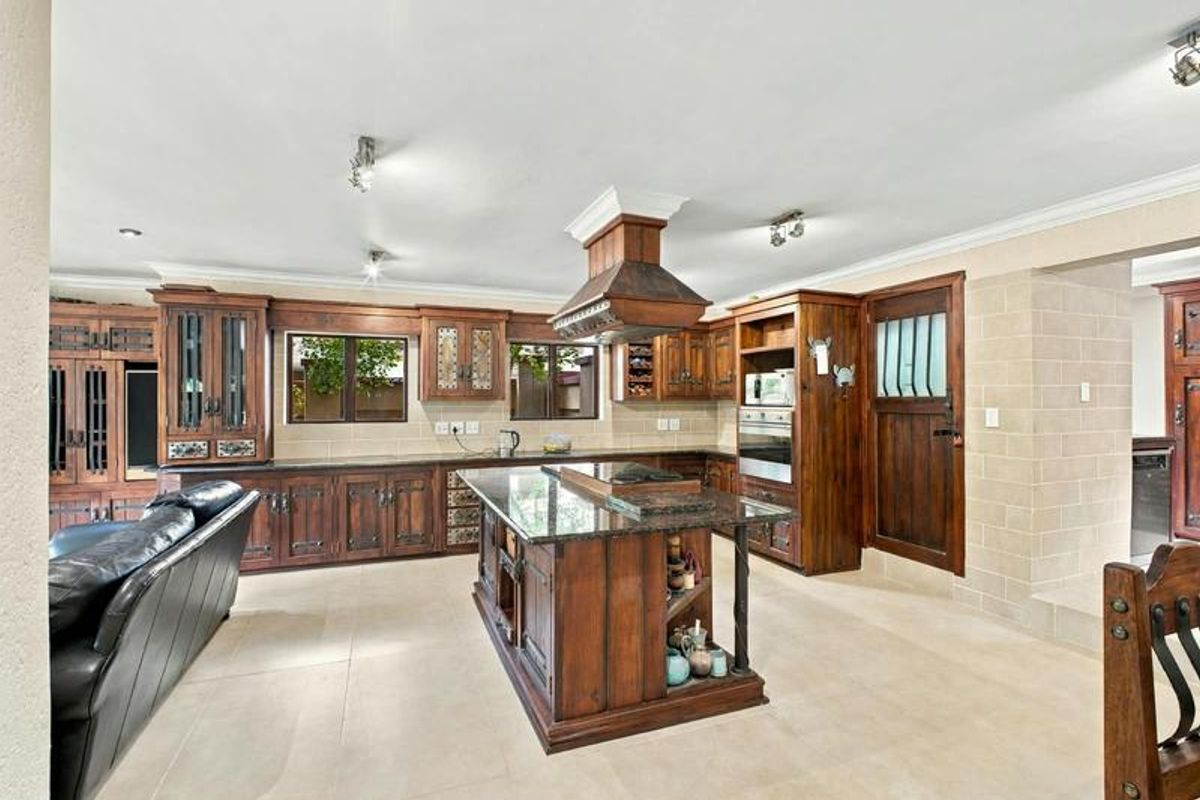 Spacious kitchen featuring custom wooden cabinetry, granite countertops, a central island with built-in cooktop, and tiled flooring throughout.