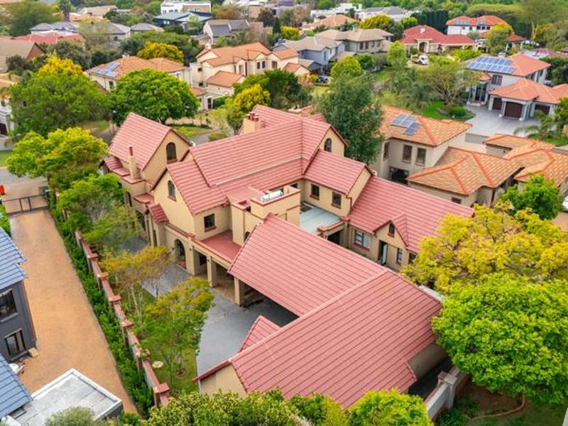 Aerial view of a large residential property featuring a multi-pitched tiled roof, paved driveway, and established garden within a suburban estate setting.