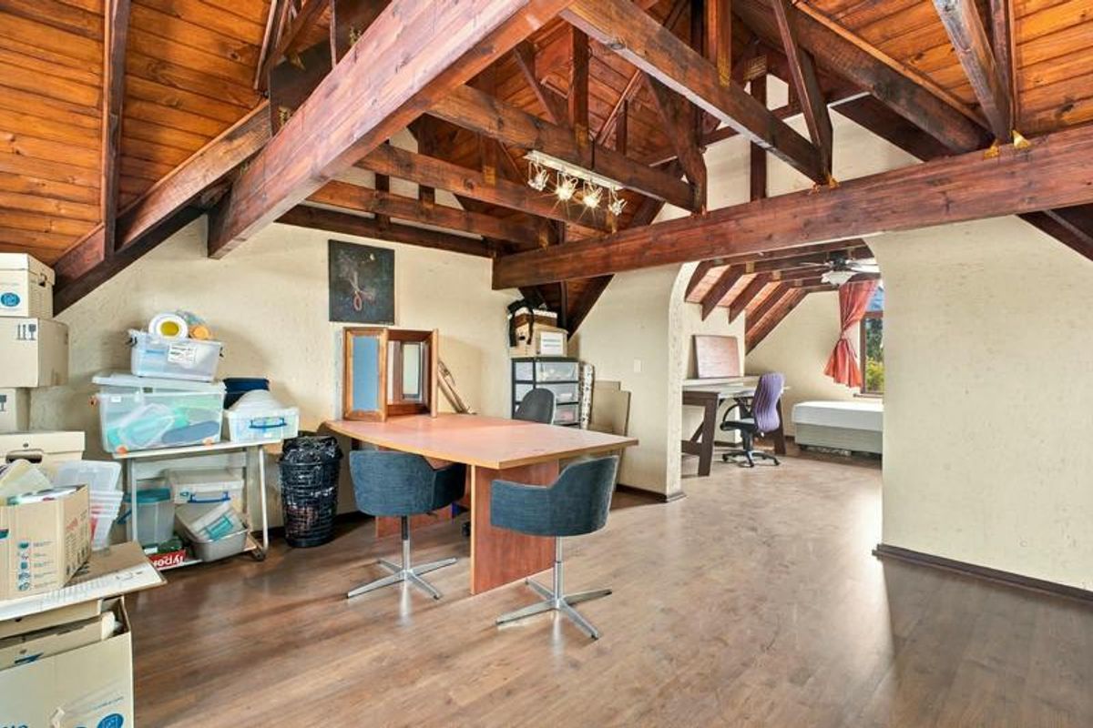 Spacious attic-style living area featuring exposed timber roof trusses, vaulted ceilings, and laminate flooring with an arched transition to an adjacent bedroom space.