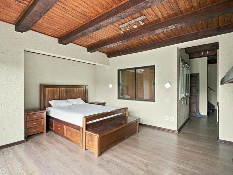 Spacious bedroom featuring exposed timber ceiling beams, laminate flooring, and textured walls, offering a rustic aesthetic with direct access to an adjoining hallway.
