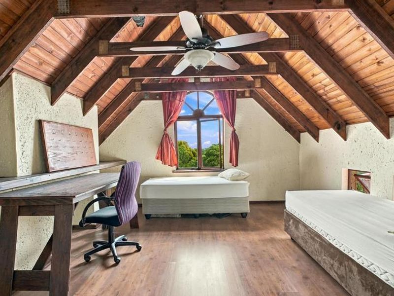 Spacious attic-style bedroom featuring exposed timber roof trusses, vaulted timber ceilings, laminate flooring, and a large arched window with natural light.