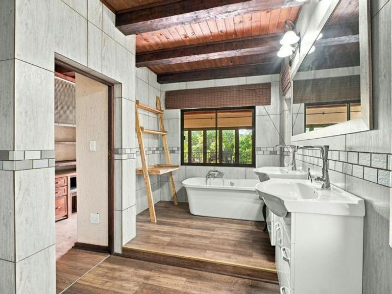 Spacious bathroom featuring a freestanding bathtub, double vanity, exposed timber ceiling beams, and modern tiled finishes with a view of the outdoors.