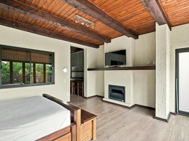 Spacious bedroom featuring exposed timber ceiling beams, a built-in fireplace, laminate flooring, and direct access to an outdoor area via a sliding glass door.