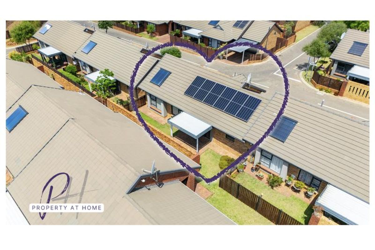 Aerial view of a townhouse complex featuring a unit with a tiled roof, installed solar panels, and a covered patio area.