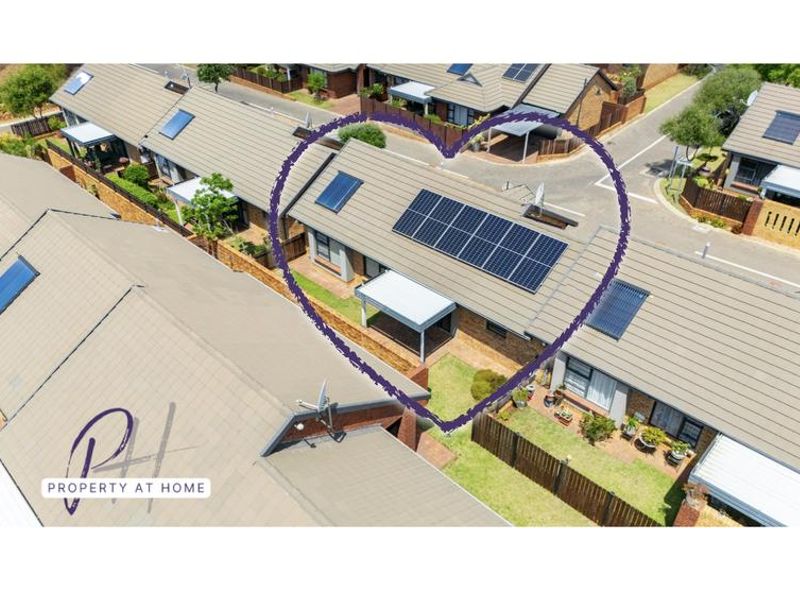Aerial view of a townhouse complex featuring a unit with a tiled roof, installed solar panels, and a covered patio area.