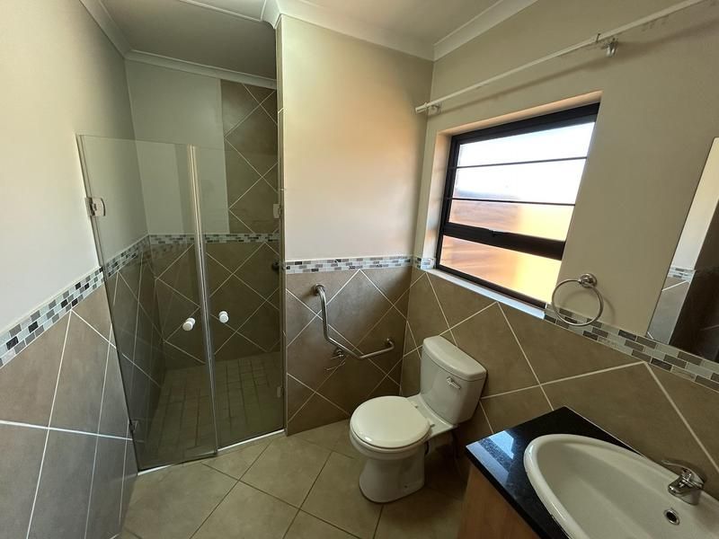 A clean and functional bathroom featuring a glass-enclosed shower, tiled walls with decorative accents, a vanity basin, and a wall-mounted grab rail.
