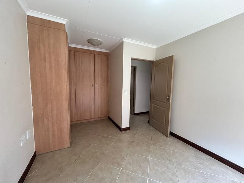 A clean, empty bedroom featuring neutral tiled flooring, built-in wooden cupboards, and a simple interior door leading to the hallway.