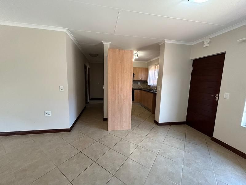 An open-plan living area featuring tiled floors and a semi-enclosed kitchen with built-in cabinetry, offering a functional and versatile layout.