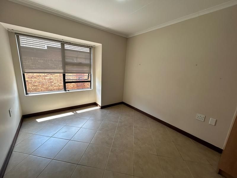 An empty bedroom featuring neutral tiled flooring, a window with a fitted roller blind, and standard electrical fixtures.