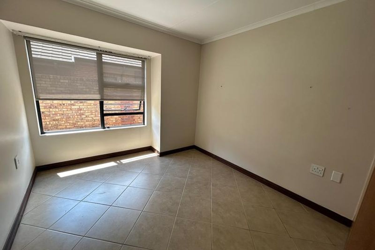 An empty bedroom featuring neutral tiled flooring, a window with a fitted roller blind, and standard electrical fixtures.