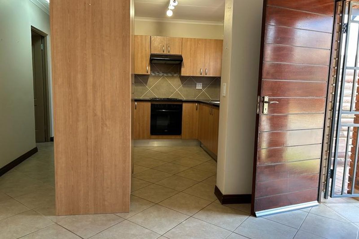 A functional kitchen featuring wood-look cabinetry, built-in oven and hob, tiled flooring, and direct access to the entrance area.