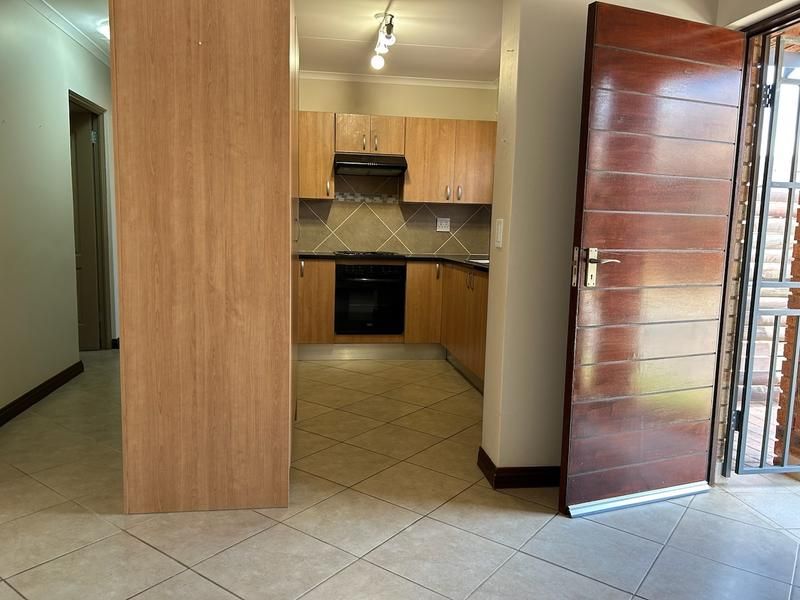 A functional kitchen featuring wood-look cabinetry, built-in oven and hob, tiled flooring, and direct access to the entrance area.