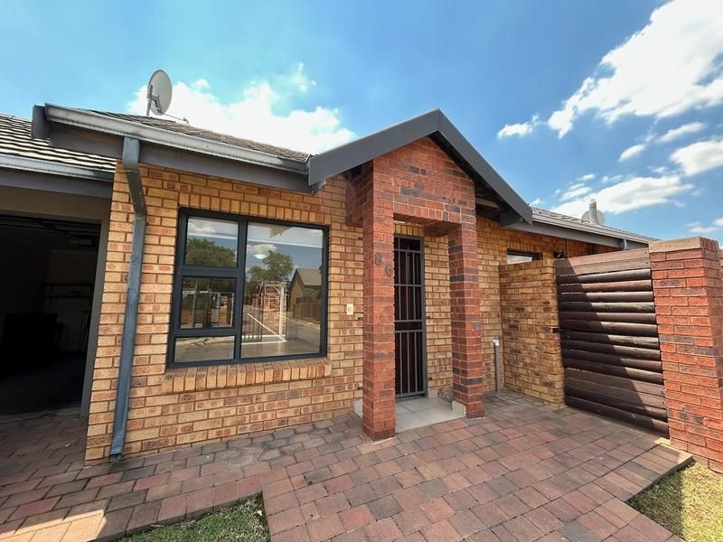 Front elevation of a face brick townhouse featuring a paved entrance, secure gate, and modern aluminium window frames under a tiled roof.
