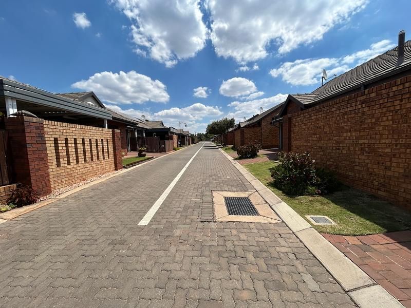 A view of the paved complex driveway lined with brick townhouse units and boundary walls under a clear blue sky.