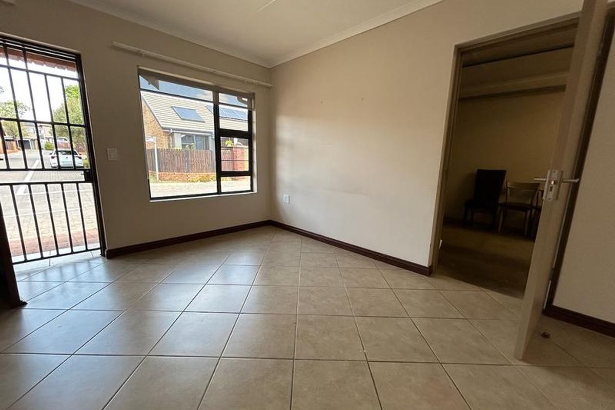 An empty living room featuring neutral tiled flooring, a security gate at the entrance, and large windows allowing for natural light.