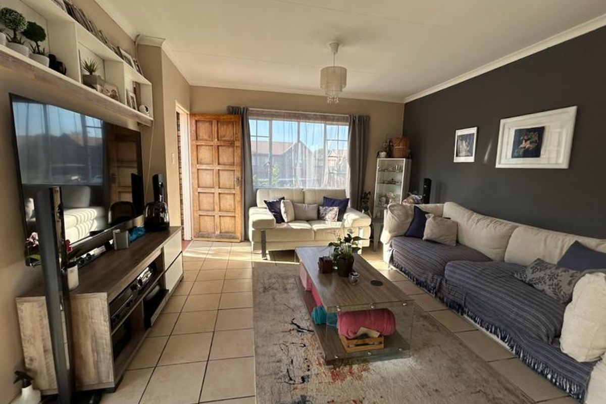 A comfortable living room featuring tiled flooring, a built-in shelving unit, and a timber entrance door, offering a functional and inviting space.