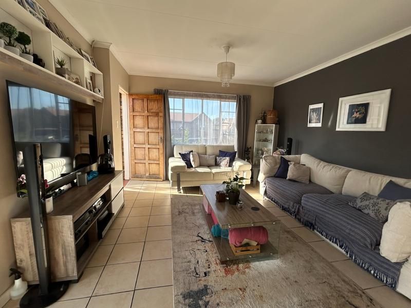 A comfortable living room featuring tiled flooring, a built-in shelving unit, and a timber entrance door, offering a functional and inviting space.