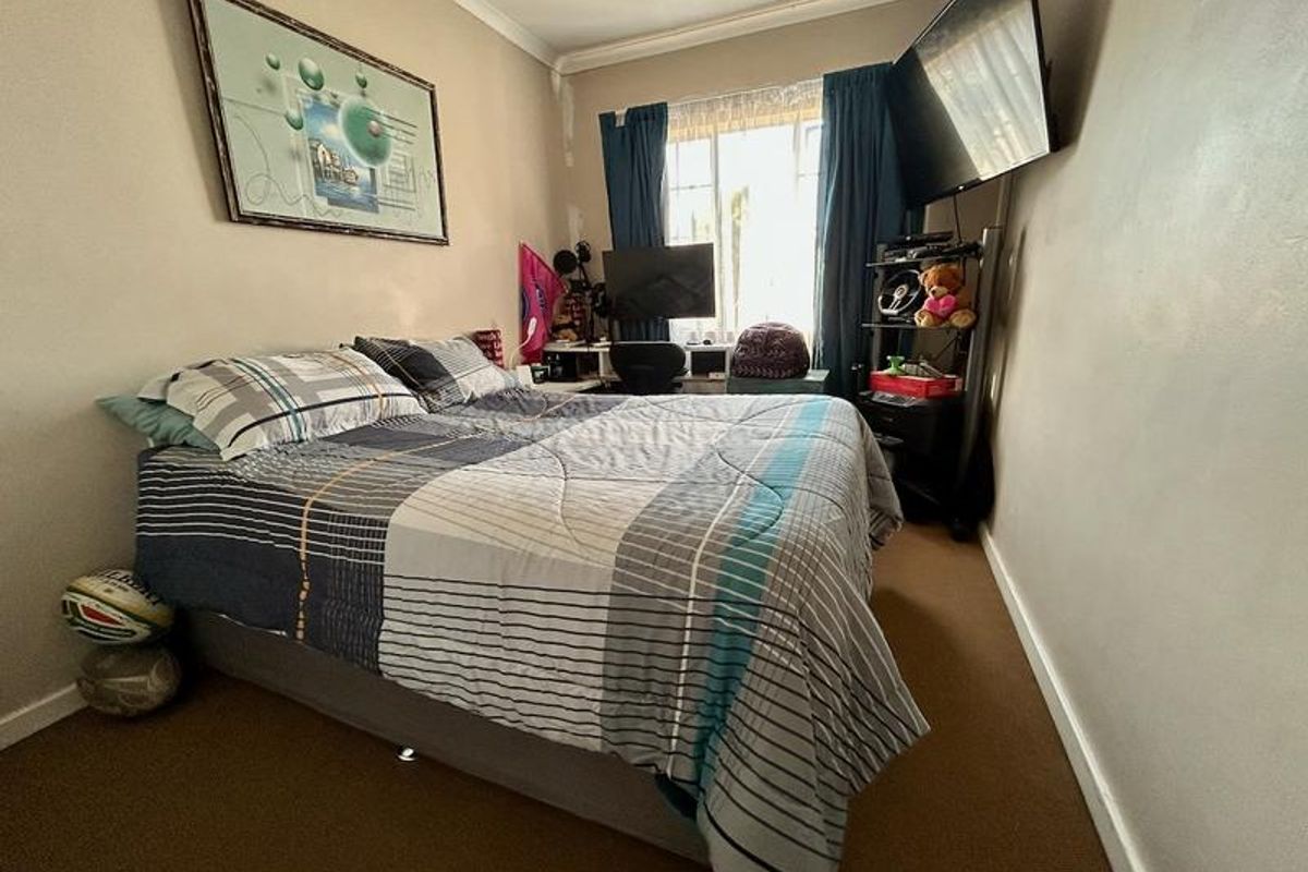 A compact bedroom featuring carpeted flooring and coved ceilings, currently showing signs of wear on the wall surfaces and window surrounds.
